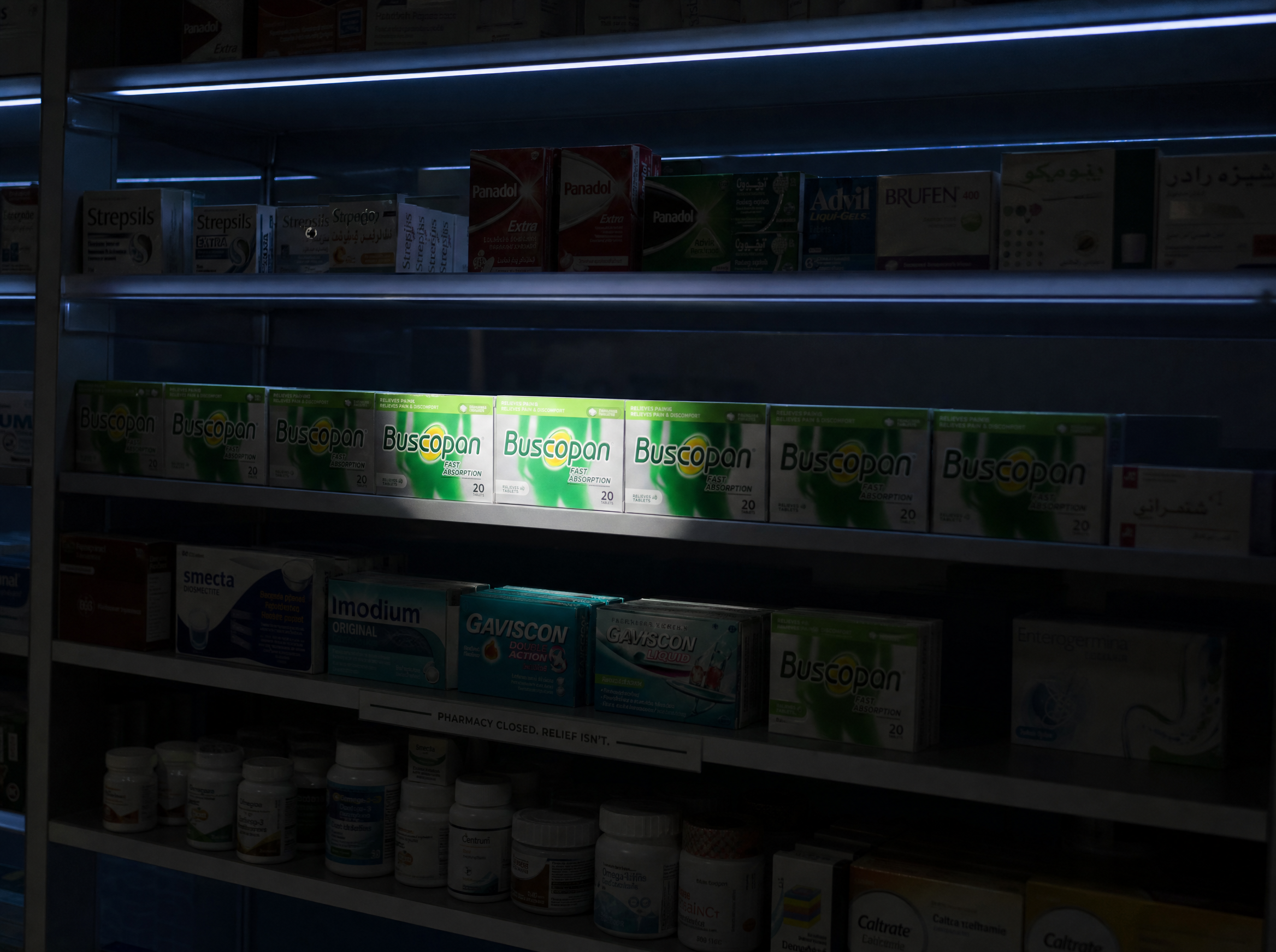 A pharmacy shelf at night with one row of Buscopan boxes lit by a phone flashlight